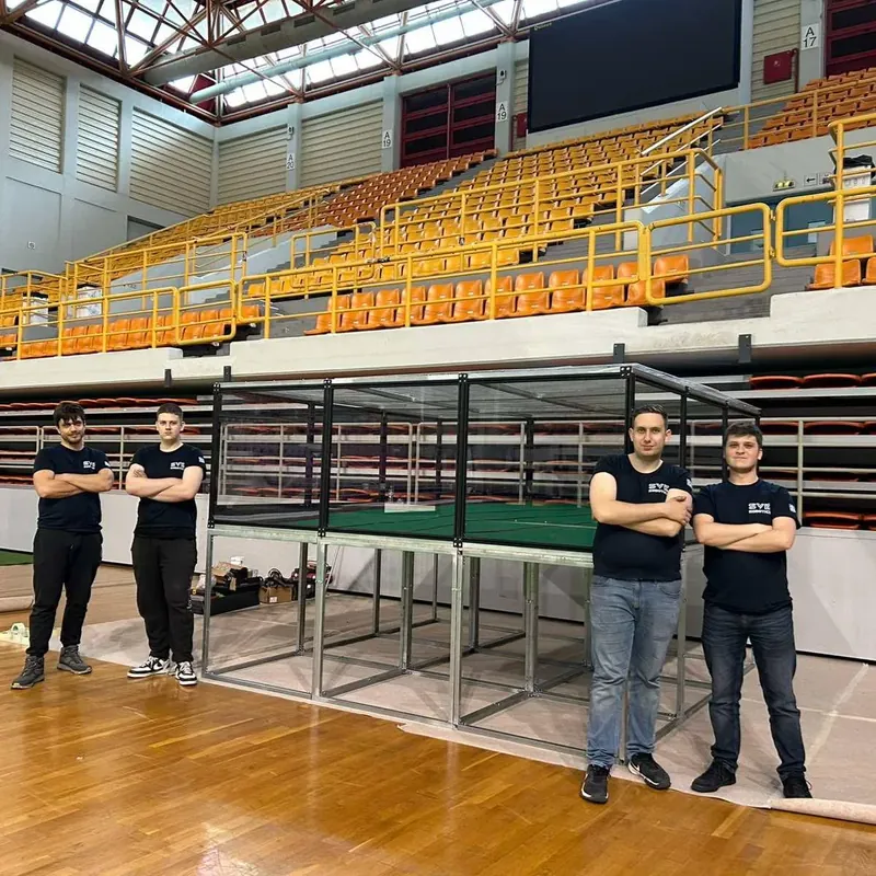 The SVK Robotics team in front of the MRC 2025 cage arena in an indoor stadium