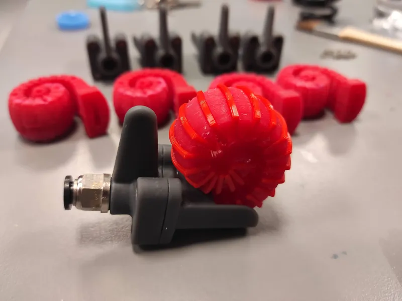 Red spiral soft actuator, unwound, beside a pneumatic fitting